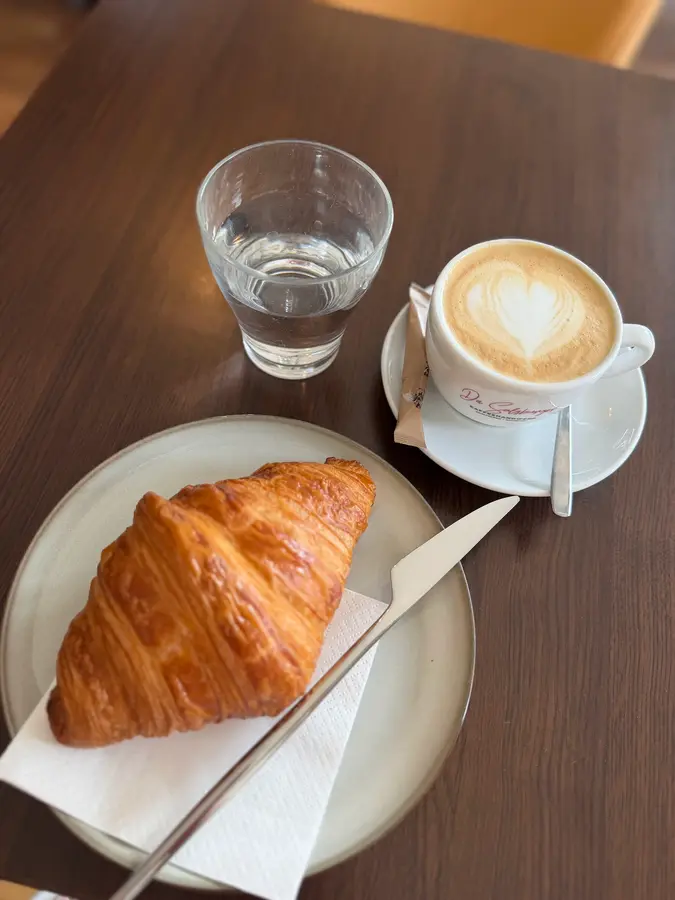 Hausgemachtes Croissant mit Cappuccino und einem Glas Wasser auf einem Holztisch