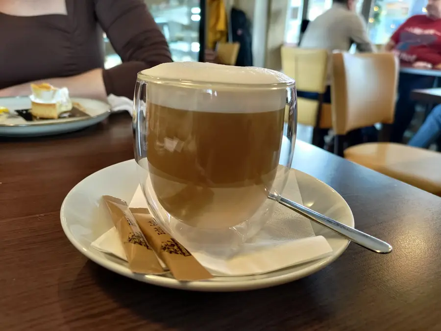 Latte macchiato im doppelwandigen Glas, im Hintergrund das Café