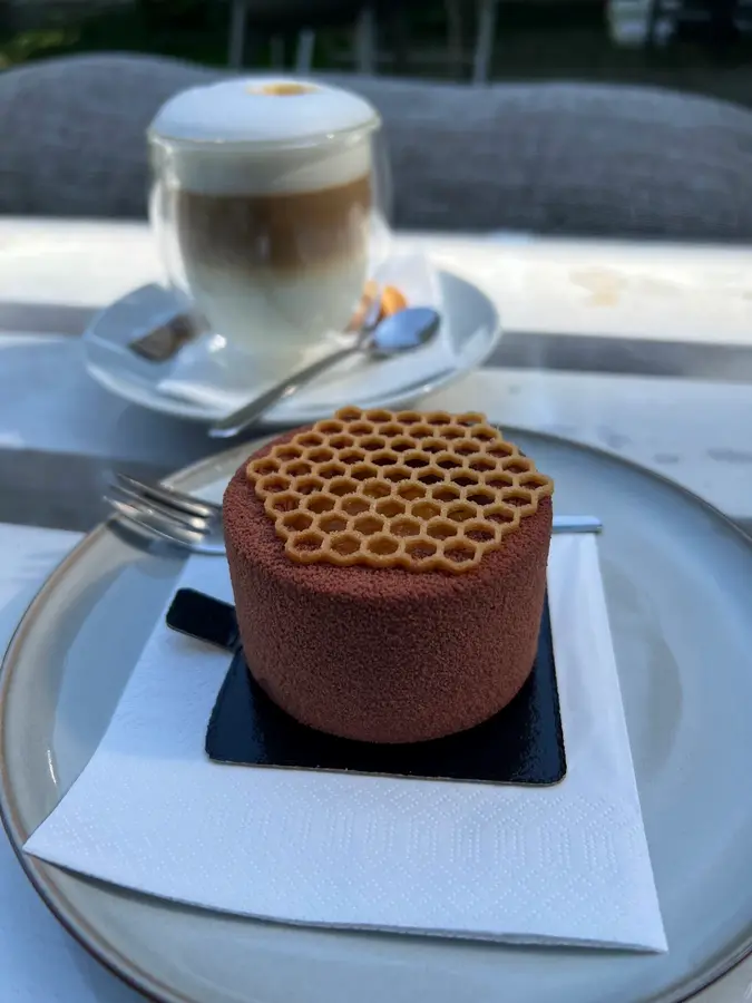 Schokoladen-Törtchen mit Wabengitter, dahinter ein Latte macchiato im Garten